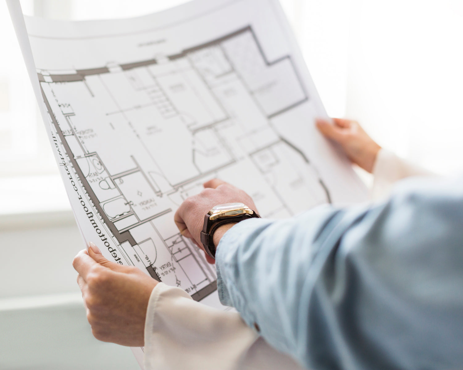 Eine Person haelt einen Architekturplan, eine andere zeigt auf ein Detail, nur Haende und weisses Papier sichtbar