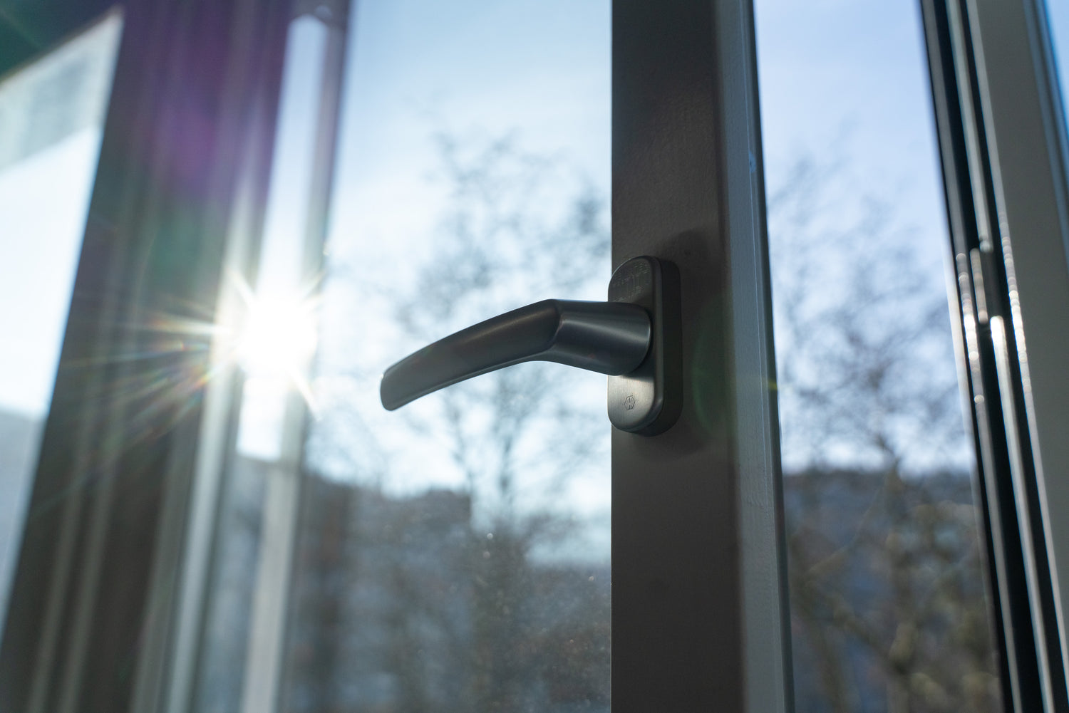 Detail eines weissen Fensters mit grauem Griff, Sonnenlicht im Hintergrund, hochwertige Verarbeitung