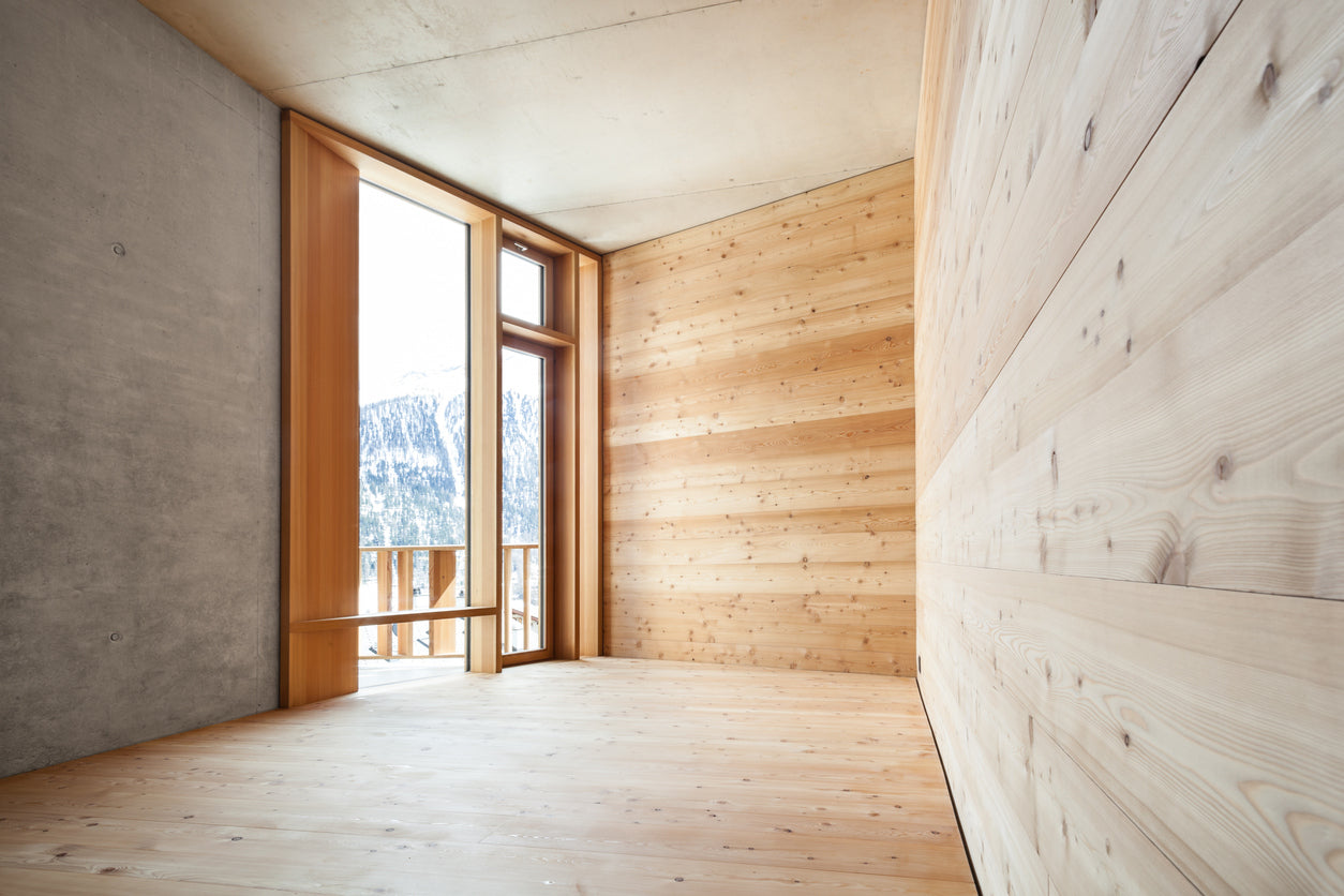 Raum mit Holzverkleidung, bodentiefe Fenster mit Ausgang zur Terrasse, Blick auf verschneite Berge, helle Holztoene
